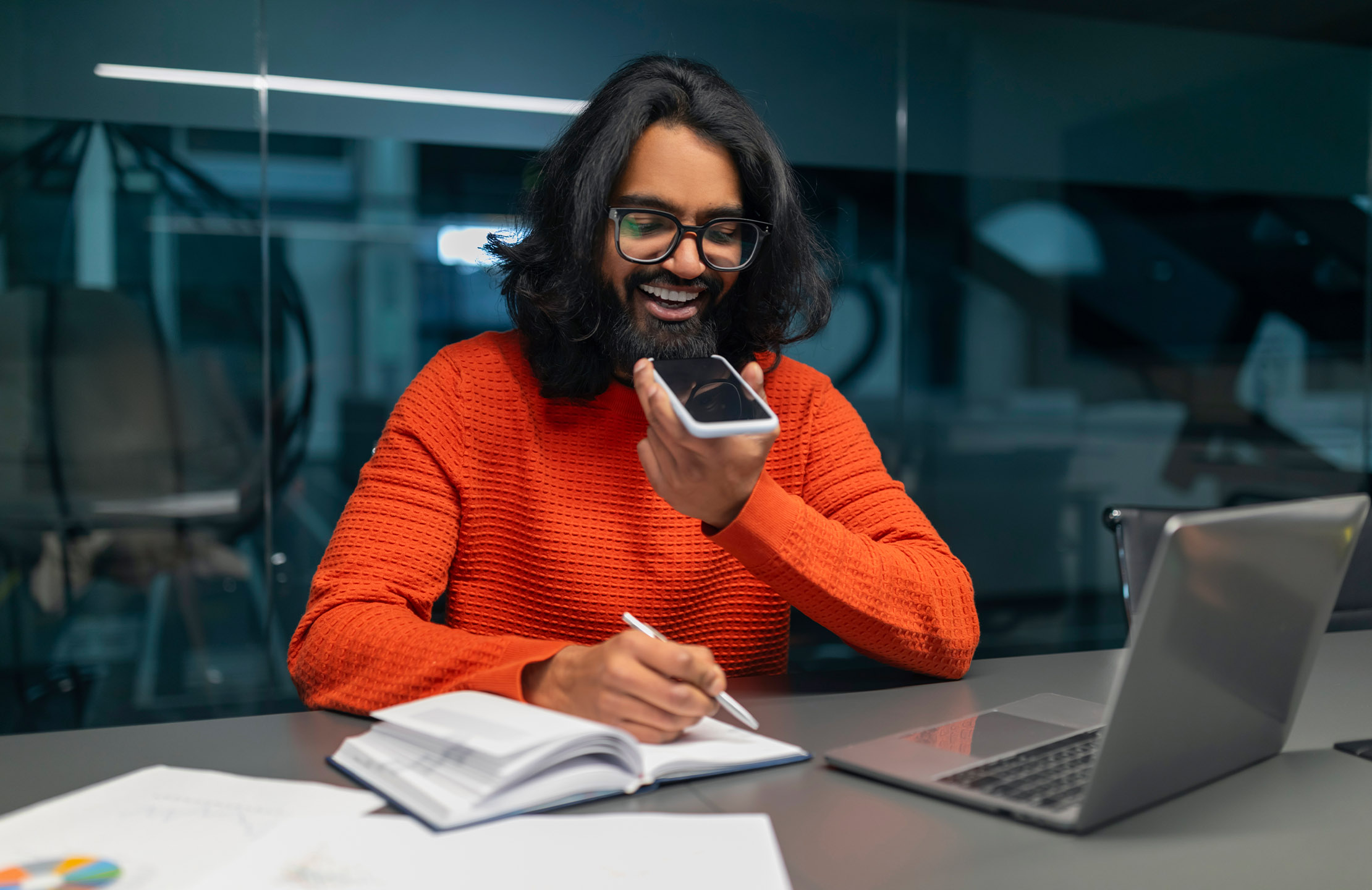 A person in an orange top talking into the speaker on their mobile phone